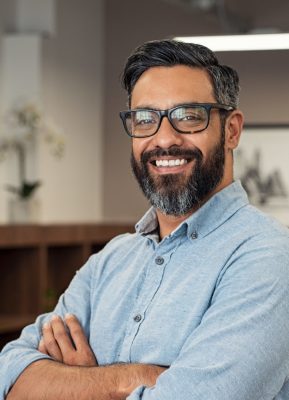 Portrait of happy mature businessman wearing spectacles and looking at camera. Multiethnic satisfied man with beard and eyeglasses feeling confident at office. Successful middle eastern business man smiling in a creative office.